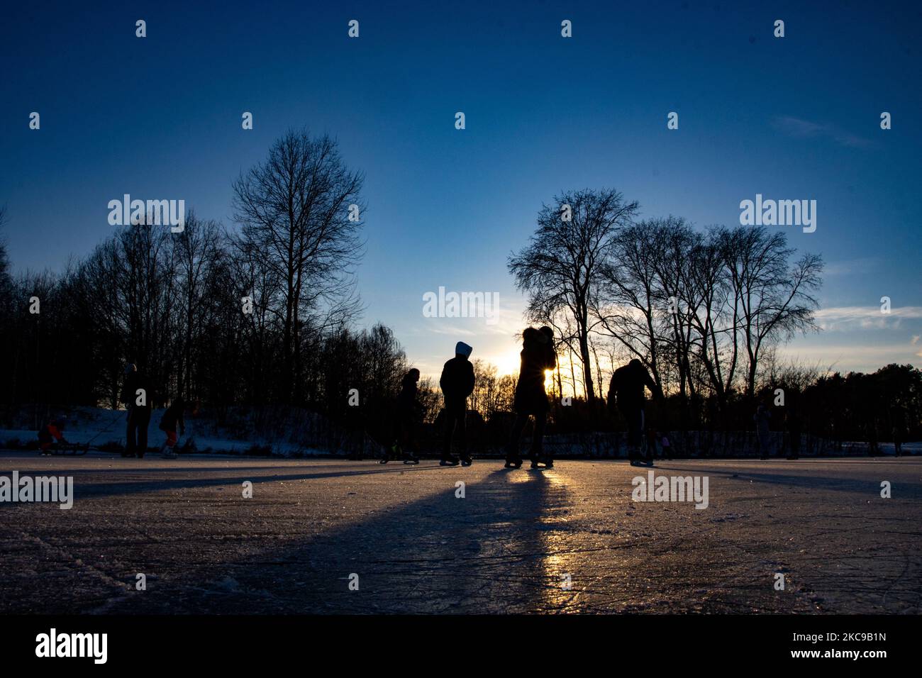 Dunkle Silhouetten von Menschen beim Eislaufen auf dem kristallklaren natürlichen gefrorenen See in der Region Nordbrabant am Nachmittag vor dem Sonnenuntergang. Eislaufrausch übernimmt die Niederlande. Die Niederländer haben viel Spaß und genießen das einwöchige, kalte Schneewetter mit Temperaturen unter Null, die dazu führen, dass Seen, Bäche, Teiche, Flüsse und Kanäle gefrieren. Im Park Meerland in der Nähe der Stadt Eindhoven haben sich die Massen an einem sonnigen Tag mit blauem Himmel abgesetzt, da es eine niederländische Tradition ist. Außerdem werden die Menschen im Freien in der eisgefrorenen Natur und der kalten Umgebung gesehen, die auf dem Eis der gefrorenen Seen spazieren gehen, p Stockfoto