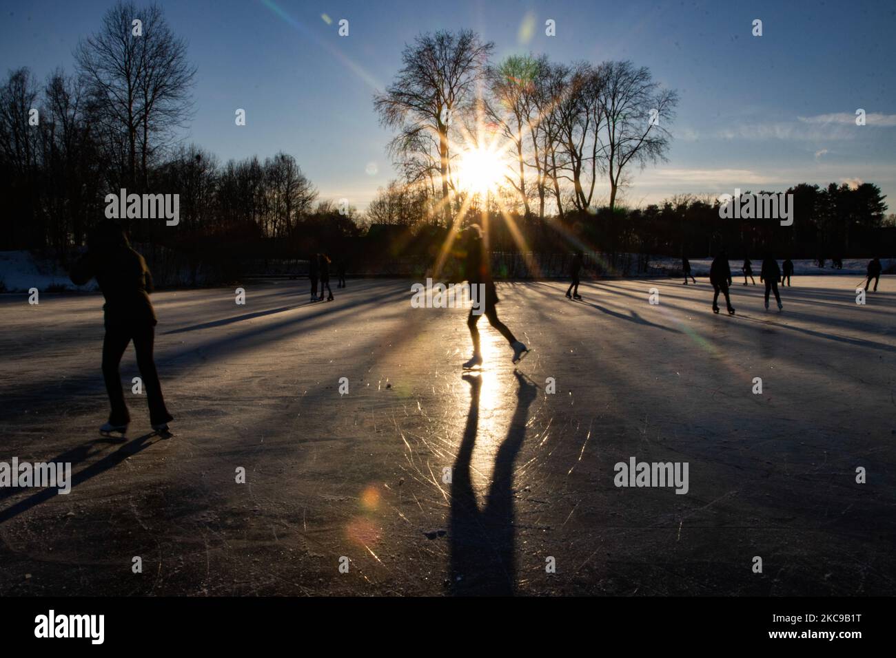 Dunkle Silhouetten von Menschen beim Eislaufen auf dem kristallklaren natürlichen gefrorenen See in der Region Nordbrabant am Nachmittag vor dem Sonnenuntergang. Eislaufrausch übernimmt die Niederlande. Die Niederländer haben viel Spaß und genießen das einwöchige, kalte Schneewetter mit Temperaturen unter Null, die dazu führen, dass Seen, Bäche, Teiche, Flüsse und Kanäle gefrieren. Im Park Meerland in der Nähe der Stadt Eindhoven haben sich die Massen an einem sonnigen Tag mit blauem Himmel abgesetzt, da es eine niederländische Tradition ist. Außerdem werden die Menschen im Freien in der eisgefrorenen Natur und der kalten Umgebung gesehen, die auf dem Eis der gefrorenen Seen spazieren gehen, p Stockfoto