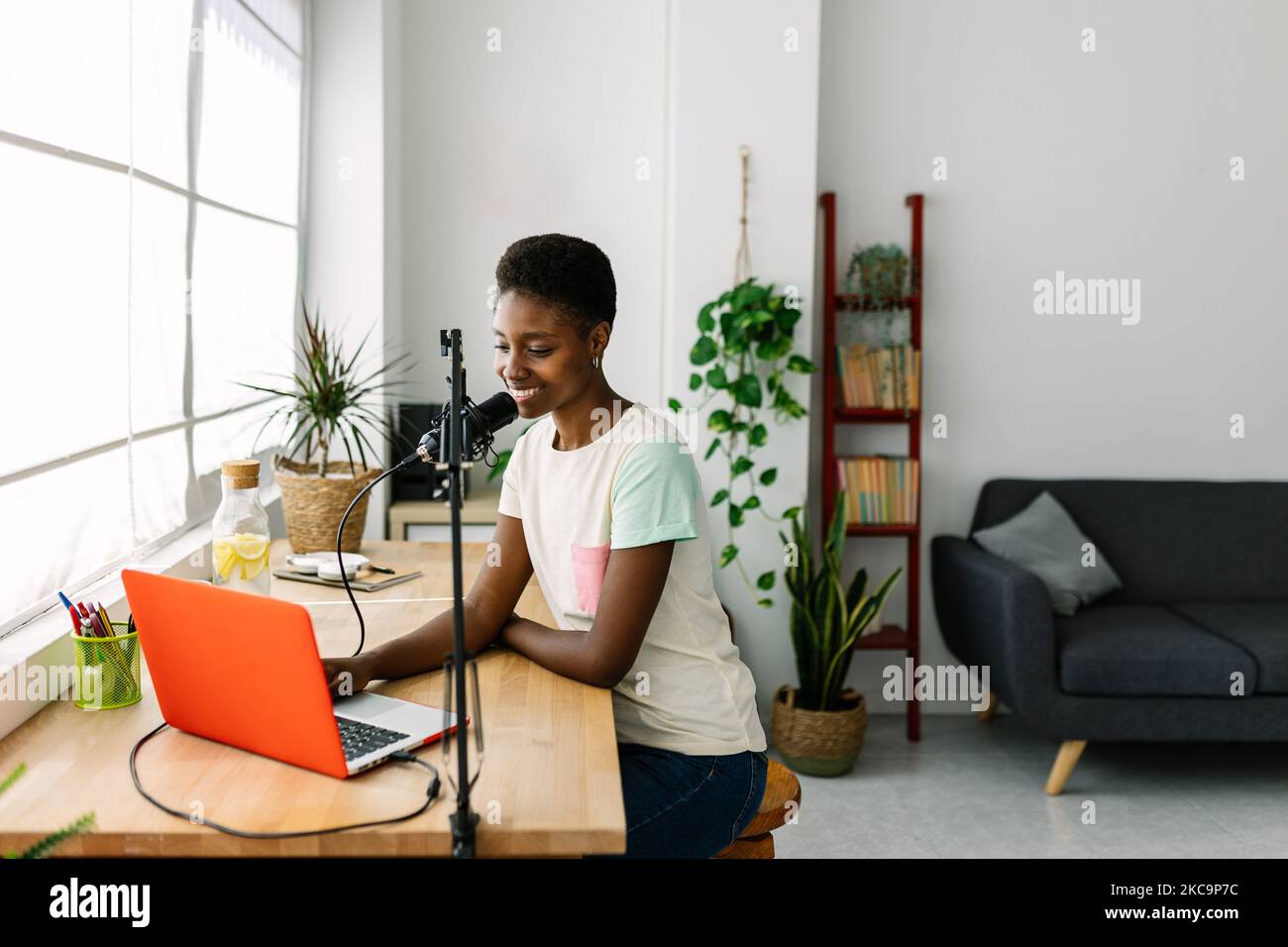 Lächelnde junge afrikanische Frau, die Podcast im modernen Studio zu Hause aufzeichnet Stockfoto