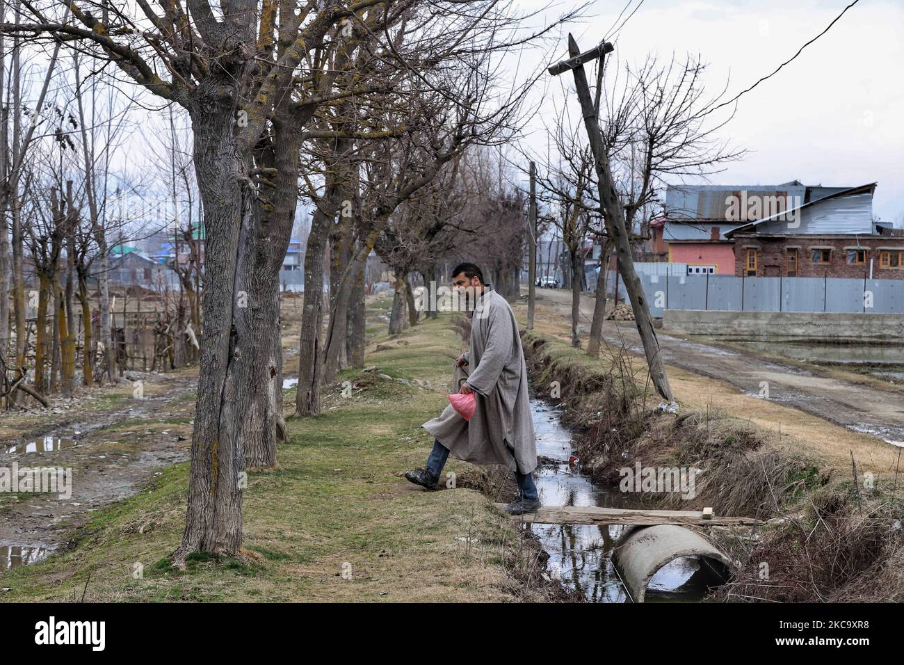 Ein Kashmiri-Mann geht am 24. Februar 2021 in der Nähe eines Wasserkanals mit einem Feran am Stadtrand von Sovore im Distrikt Baramulla, jammu und Kaschmir, Indien, spazieren. Rashtriya Bajrang Dal, die rechtsgerichteten Hindu-Organisation, hat ein Verbot des Tragens von Pher in Jammu und Kaschmir gefordert. Dal behauptete, dass es von Militanten missbraucht wurde, um Angriffe auf Regierungskräfte durchzuführen. (Foto von Nasir Kachroo/NurPhoto) Stockfoto