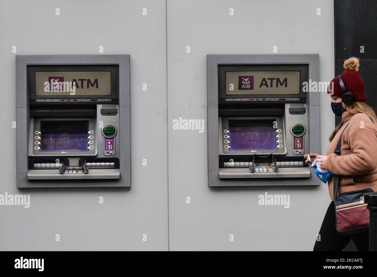 Eine Frau mit Gesichtsmaske kommt während der COVID-19-Sperre auf Level 5 an einem AIB-Geldautomaten im Stadtzentrum von Dublin vorbei. Die Bank of Ireland gab heute die Schließung von 103 Filialen in ganz Irland bekannt, da die Beschleunigung des digitalen Bankwesens nun seinen „kritischen Punkt“ erreicht hat. Insgesamt werden 88 Filialen in der Republik Irland schließen, die 169 verlassen werden, und 15 Filialen in Nordirland werden die 13 schließen. Am Montag, den 1. März 2021, in Dublin, Irland. (Foto von Artur Widak/NurPhoto) Stockfoto