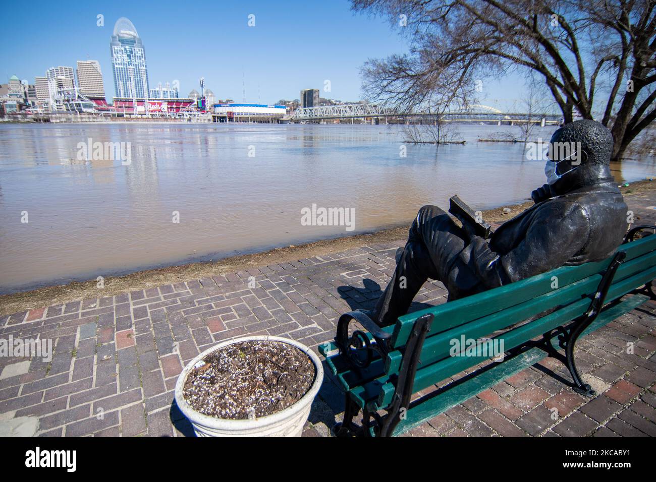 Eine Bronzestatue eines Mannes, der ein Buch mit einer Maske liest, sitzt am Ufer des Ohio River, als einige Straßen und Geschäfte in einigen niedrig gelegenen Gebieten entlang der nach Tagen des Regens dicht gefüllten lokalen Wasserstraßen über ihre Ufer schließen mussten, Donnerstag, 4. März 2021, In Cincinnati, Ohio, USA. (Foto von Jason Whitman/NurPhoto) Stockfoto