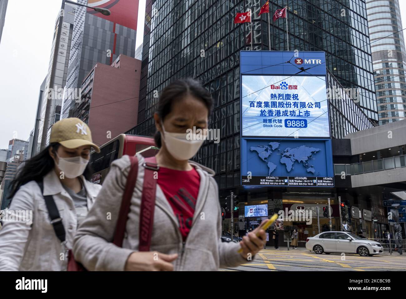 Fußgänger gehen über eine Straße an einem Bildschirm vorbei, auf dem die Notierung von Baidu Inc. An der Börse von Hongkong in Hongkong, China, am Dienstag, dem 23. März 2021, angezeigt wird. Baidus Aktienangebot in Hongkong markiert heute ein unwahrscheinliches Wiederaufleben für founderÂ Robin Li, der sich nach dem Verschwendung eines beinahe-Monopols bei der Suche wieder zur Relevanz in der chinesischen Technologiebranche zurückgeschlagen hat. (Foto von Vernon Yuen/NurPhoto) Stockfoto