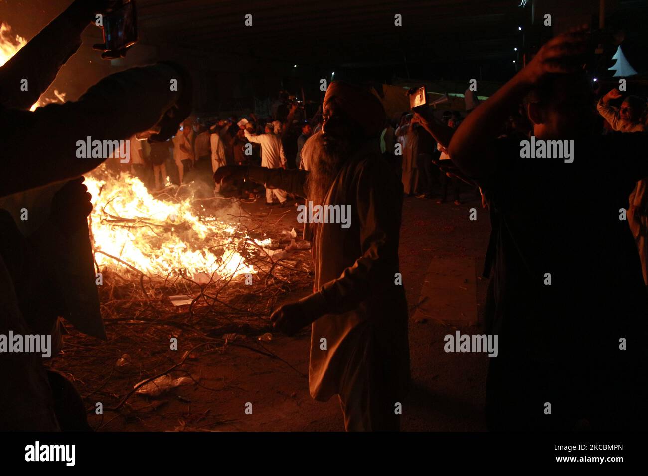 Während eines Rituals namens „Holika Dahan“, das im Rahmen der Holi-Feierlichkeiten an der Grenze zwischen Delhi und Uttar Pradesh in der Nähe von Ghazipur, am Stadtrand von Neu Delhi, stattfand, tanzen die Bauern, während sie Kopien der Agrargesetze in einem Lagerfeuer verbrennen. Indien am 28. März 2021. (Foto von Mayank Makhija/NurPhoto) Stockfoto