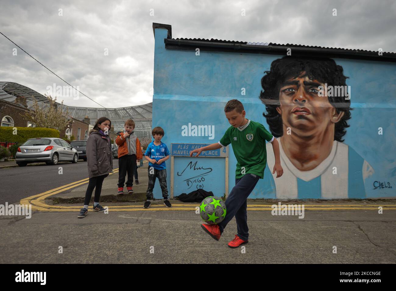 Johnny Figo Murphy, 9 Jahre alt, zeigt seine Fußballschuhe vor einem neuen Wandgemälde von CHELS (Chelsea Jacobs, ein in Dublin lebender amerikanischer Künstler), der Diego Maradona, einen der größten Spieler in der Geschichte des Fußballs, vertritt. Am Dienstag, den 13. April 2021, in Dublin, Irland. (Foto von Artur Widak/NurPhoto) Stockfoto