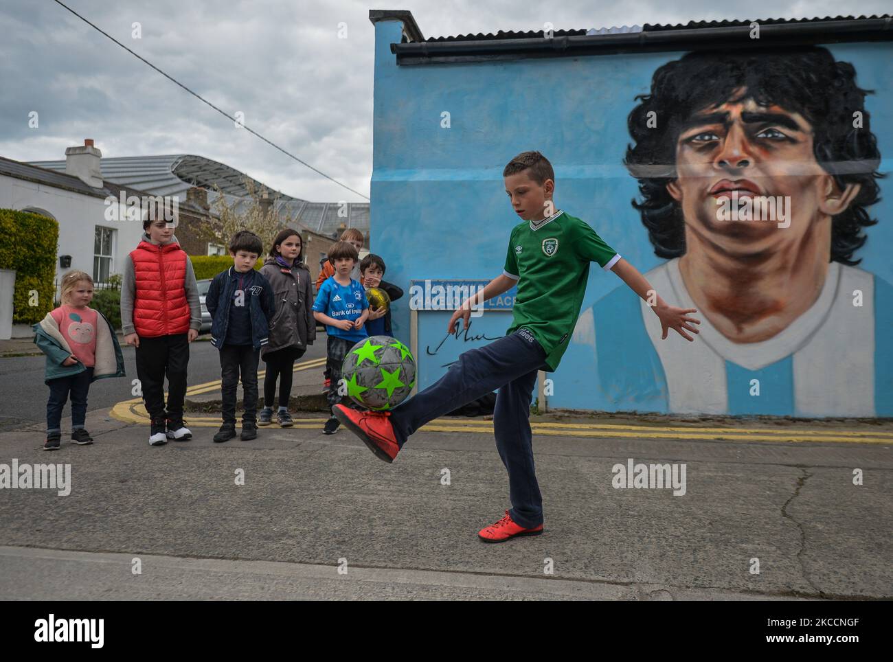 Johnny Figo Murphy, 9 Jahre alt, zeigt seine Fußballschuhe vor einem neuen Wandgemälde von CHELS (Chelsea Jacobs, ein in Dublin lebender amerikanischer Künstler), der Diego Maradona, einen der größten Spieler in der Geschichte des Fußballs, vertritt. Am Dienstag, den 13. April 2021, in Dublin, Irland. (Foto von Artur Widak/NurPhoto) Stockfoto