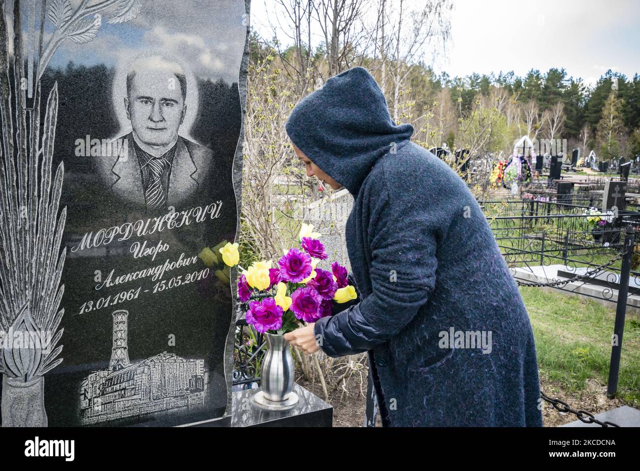 Die Frau hinterlässt am 24. April 2021 Blumen im Grab eines Verwandten auf dem Slavutych-Friedhof in der Ukraine. Ein Bild des Reaktors Tschernobyl Nummer 4 ist in seinen Grabstein eingemeißelt, weil er als Arbeiter im Elektrowerk tätig war. (Foto von Celestino Arce/NurPhoto) Stockfoto