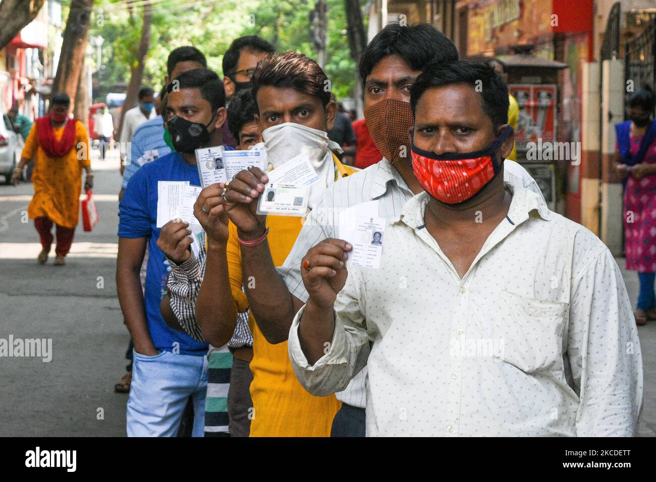 Menschen mit Maske zeigen ihren wählerausweis, als sie sich während der Phase der Wahlen zur Versammlung in Westbengalen am 26. April 2021 in Kalkutta, Indien, 7. vor einem Wahllokal anstellten. (Foto von Debarchan Chatterjee/NurPhoto) Stockfoto