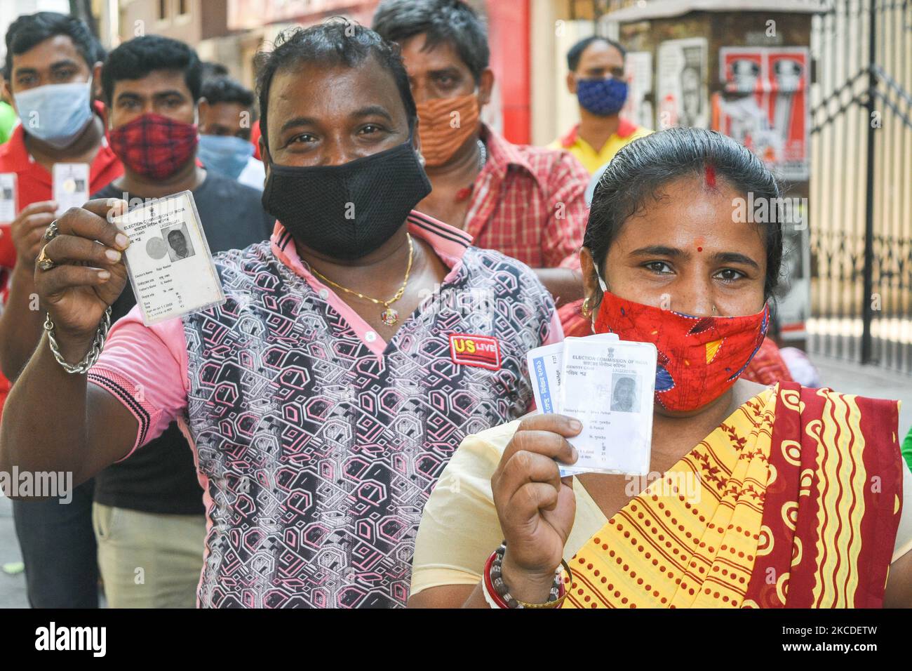 Menschen mit Maske zeigen ihren wählerausweis, als sie sich während der Phase der Wahlen zur Versammlung in Westbengalen am 26. April 2021 in Kalkutta, Indien, 7. vor einem Wahllokal anstellten. (Foto von Debarchan Chatterjee/NurPhoto) Stockfoto