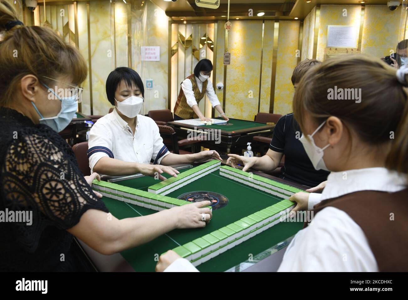 Menschen mit Gesichtsmasken spielen Mahjong an einem Mahjong-Tisch, während Arbeiter am 28. April 2021 in einer Mahjong Hall in Hongkong, China, andere Tische reinigen. Hongkong hat seine Mahjong Hall über acht Monate geschlossen und wird morgen wieder eröffnet. Hongkong hat begonnen, seine Covid-19-Beschränkungen zu lockern, nachdem Hongkong neue Fallzahlen bei Low Case gesehen und sein Impfprogramm gestartet hat. (Foto von Vernon Yuen/NurPhoto) Stockfoto