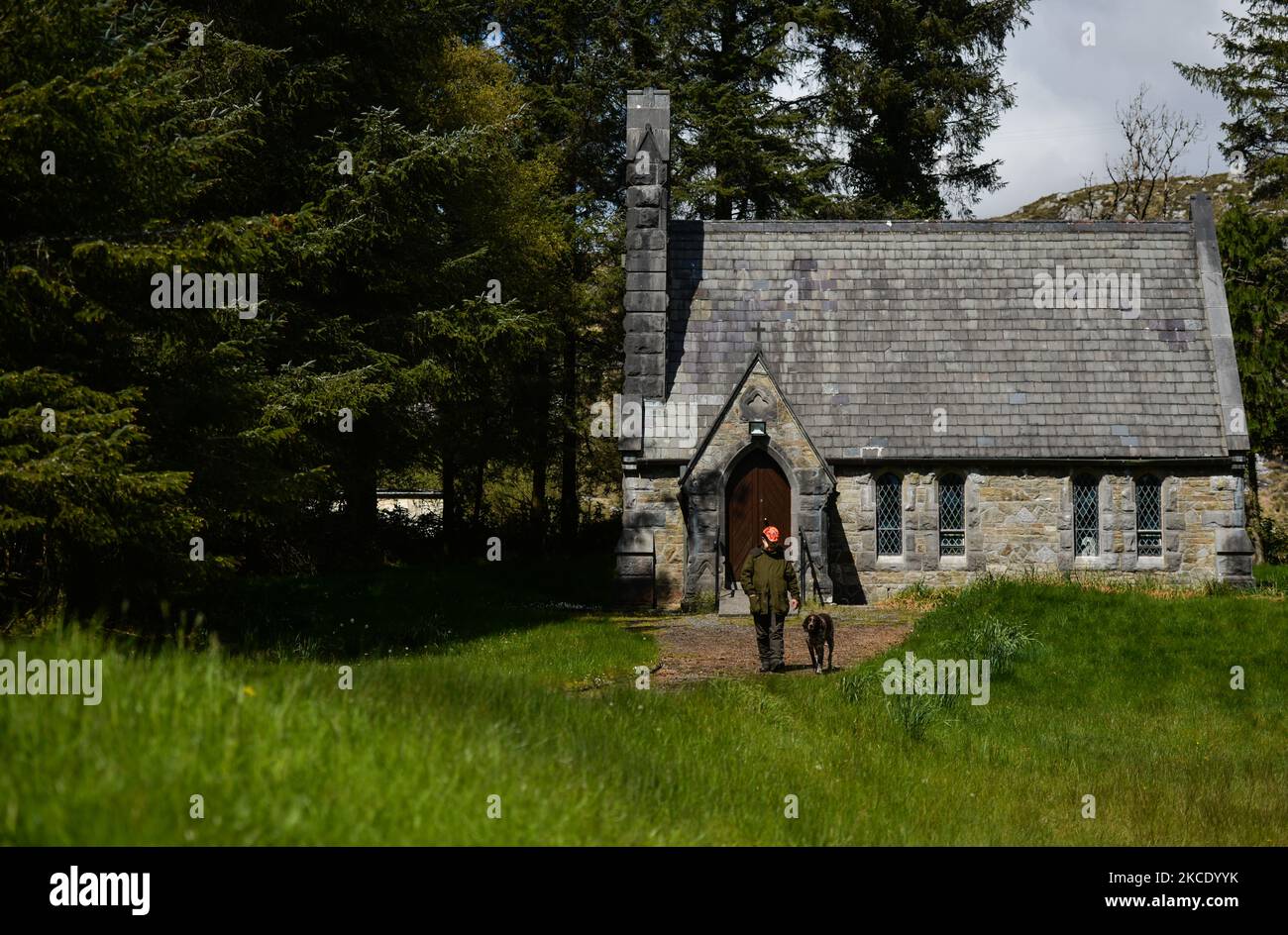 Pater Krzysztof Sikora mit seinem Hund 'Rambo' vor der Ballynahinch Kirche in Emlaghdauroe, Connemara. Diese ehemalige Kirche der irischen Kirche aus dem Jahr 1865, heute bekannt als St. Hubert, der schutzpatron der Jäger, liegt in der spektakulärsten Landschaft der Berge, Moor und Seen. Die Gemeinde Roundstone gilt geografisch als die größte Gemeinde Irlands und erstreckt sich von den Stränden von Gurteen bis zu den zwölf Bens und dem Mám Tuirc-Gebirge. Bis zum 1990s wurde die Pfarrei von drei Priestern gedient, jetzt gibt es nur noch einen, der fünf Kirchen betreut. Der derzeitige Pfarrer, ein polnischer gebürtiger Pater Krzysz Stockfoto