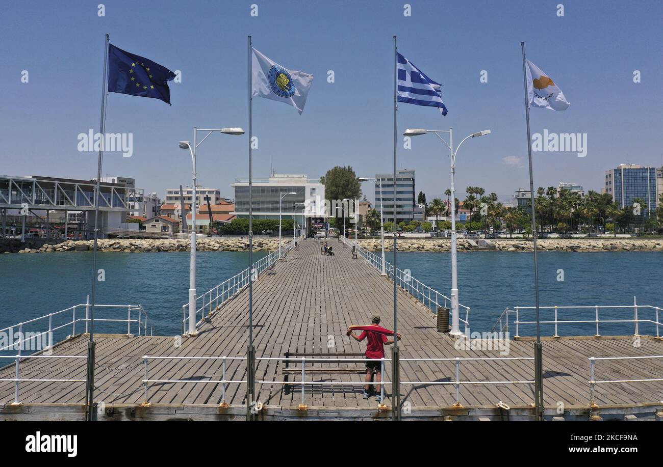 Ein Mann nimmt sich die Handtücher, nachdem er auf einem Pier mit Flaggen der EU, Limassol, Griechenlands und Zyperns im Mittelmeer-Hafen von Limassol geschwommen ist. Zypern, Donnerstag, 27. Mai 2021. Die Europäische Kommission hat der Republik Zypern 124 Millionen Euro übertragen. Dies ist die siebte Tranche im Rahmen des SURE-Programms, das von der Europäischen Union während der Coronavirus-Pandemie entwickelt wurde. Die Mittel, die Zypern aus der EU erhält, werden verwendet, um einen Teil der Gehälter der Arbeitnehmer jener Unternehmen zu bezahlen, die während der Sperrung geschlossen wurden. (Foto von Danil Shamkin/NurPhoto) Stockfoto