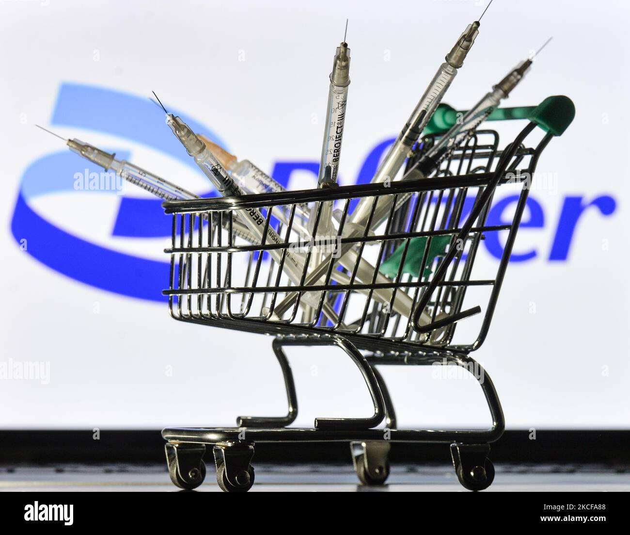Medizinische Spritzen im Mini-Einkaufswagen sind vor dem Pfizer-Logo auf einem Bildschirm zu sehen. Am Freitag, den 28. Mai 2021, in Dublin, Irland. (Foto von Artur Widak/NurPhoto) Stockfoto