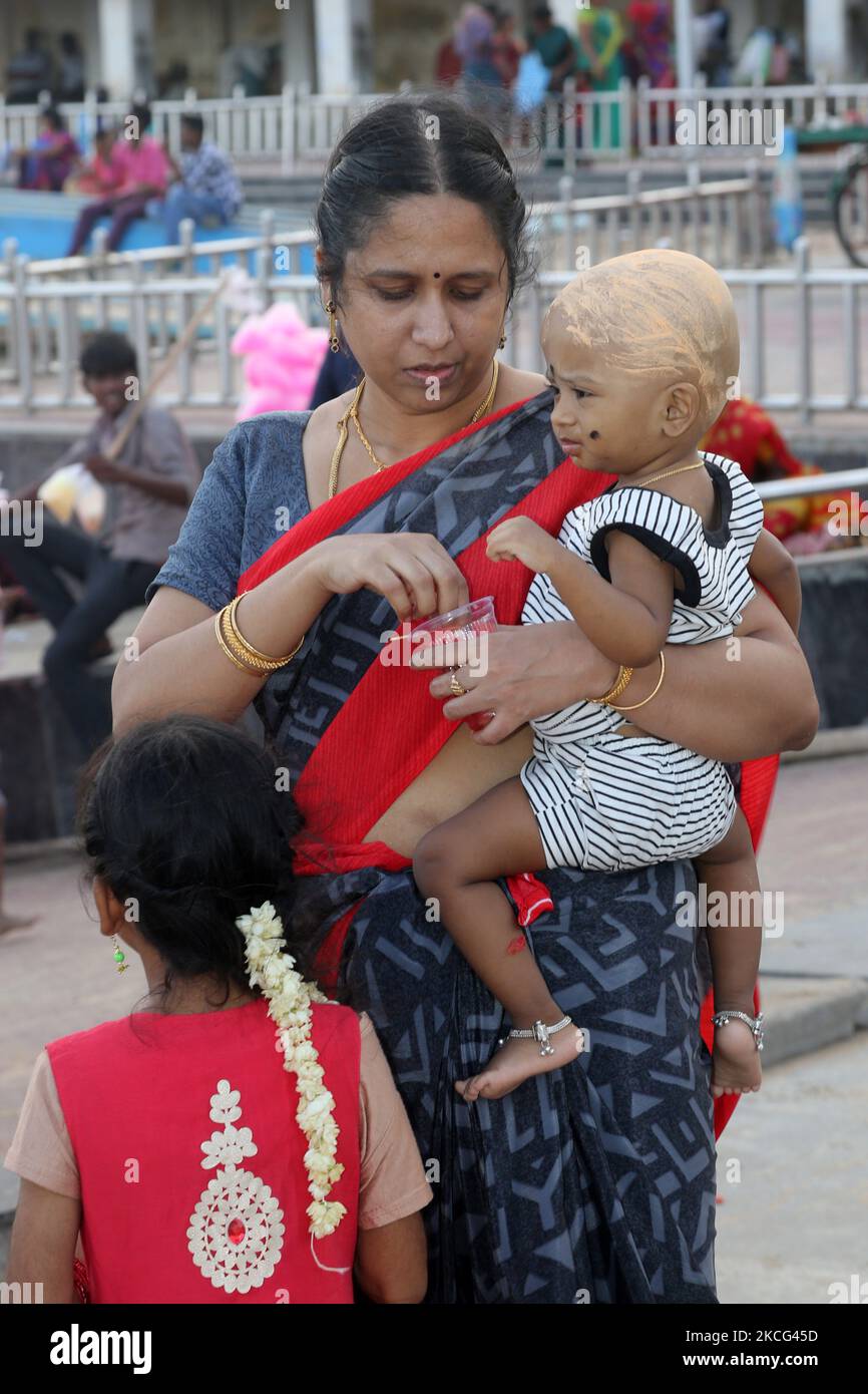 Frau hält ihr Kind, dessen Kopf im Rahmen eines Rituals im Thiruchendur