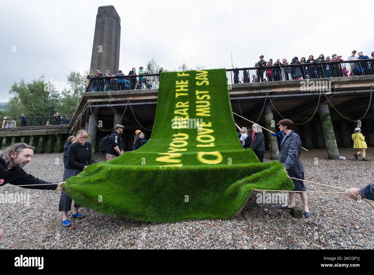 LONDON, VEREINIGTES KÖNIGREICH - 25. JUNI 2021: Aktivisten des Extinction Rebellion tragen ein Banner mit einer auf lebendigem Gras gewachsenen Botschaft am Ufer der Themse vor der Tate Modern, um am 25. Juni 2021 in London, England, auf die klimatischen und ökologischen Notsituationen aufmerksam zu machen. Das von den gefeierten Künstler-Aktivisten Ackroyd & Harvey geschaffene Banner mit einem Appell des Booker-Preisträgers Ben Okri ruft Regierungen auf der ganzen Welt dazu auf, im Hinblick auf den Gipfel COP26 mit Dringlichkeit zu handeln, um den durch die globale Erwärmung verursachten Klima- und ökologischen Kollaps zu verhindern. (Foto von Wiktor Szymanowicz/NurPhoto) Stockfoto