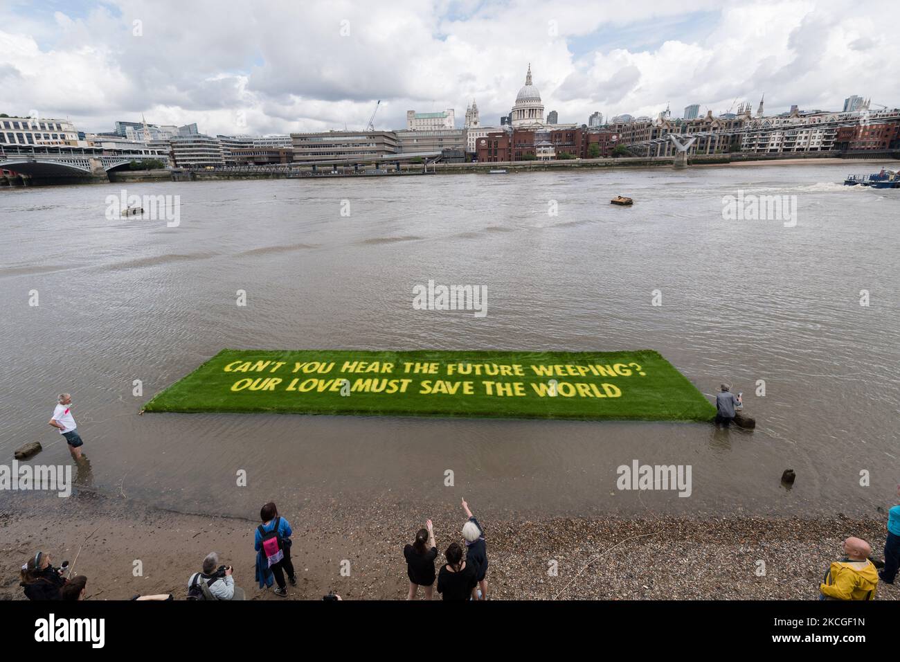 LONDON, VEREINIGTES KÖNIGREICH - 25. JUNI 2021: Ein Banner mit einer auf lebendigem Gras gewachsenen Botschaft, das von XR Writers Rebel in Auftrag gegeben wurde, schwebt am 25. Juni 2021 auf der Themse vor der Tate Modern, um auf die klimatischen und ökologischen Notsituationen in London, England, aufmerksam zu machen. Das von den gefeierten Künstler-Aktivisten Ackroyd & Harvey geschaffene Banner mit einem Appell des Booker-Preisträgers Ben Okri ruft Regierungen auf der ganzen Welt dazu auf, im Hinblick auf den Gipfel COP26 mit Dringlichkeit zu handeln, um den durch die globale Erwärmung verursachten Klima- und ökologischen Kollaps zu verhindern. (Foto von Wiktor Szymanowicz/NurPhoto) Stockfoto