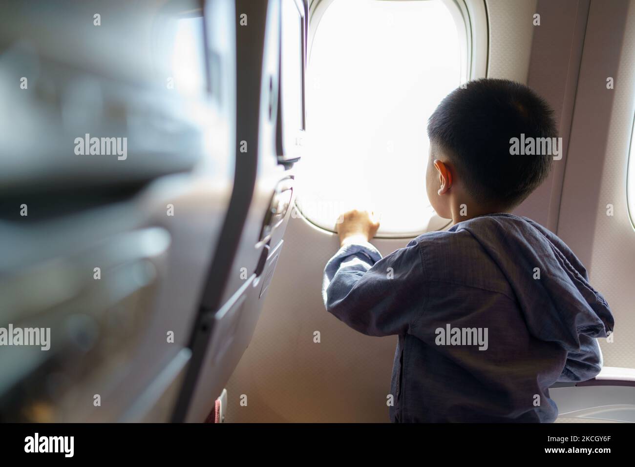 Asiatische Kinder blicken auf den Himmel und die Wolken außerhalb des Flugzeugfensters, während sie auf dem Flugzeugsitz sitzen. Stockfoto