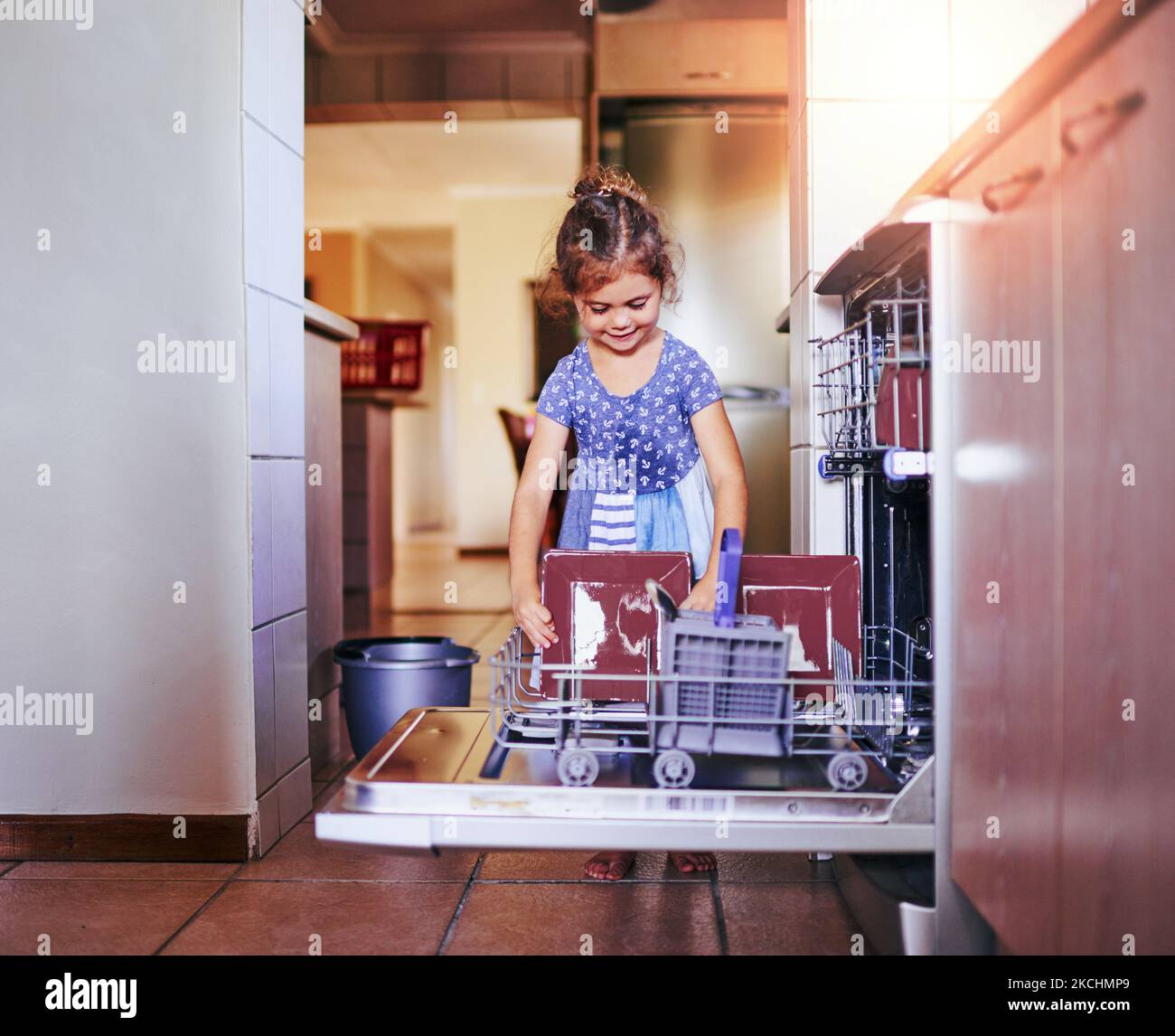 Shes eine gute kleine Haushälterin. Ein entzückendes kleines Mädchen, das die Spülmaschine zu Hause alleine beladen hat. Stockfoto