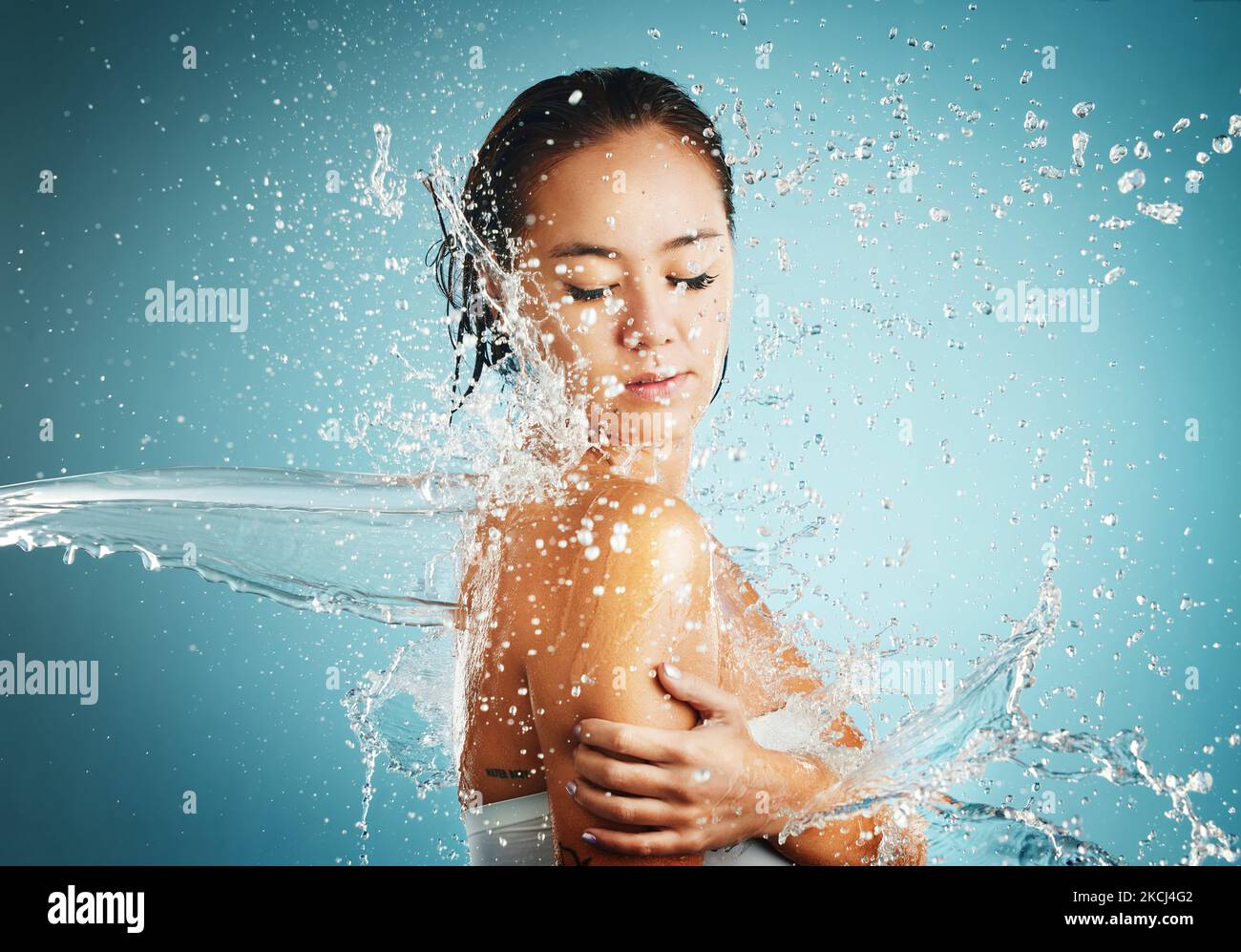 Wasser, Spritzer und Hygiene mit einer Frau, die im Studio auf blauem Hintergrund wascht oder putzt. Bad, Reinigung und Hautpflege mit einem attraktiven jungen Stockfoto