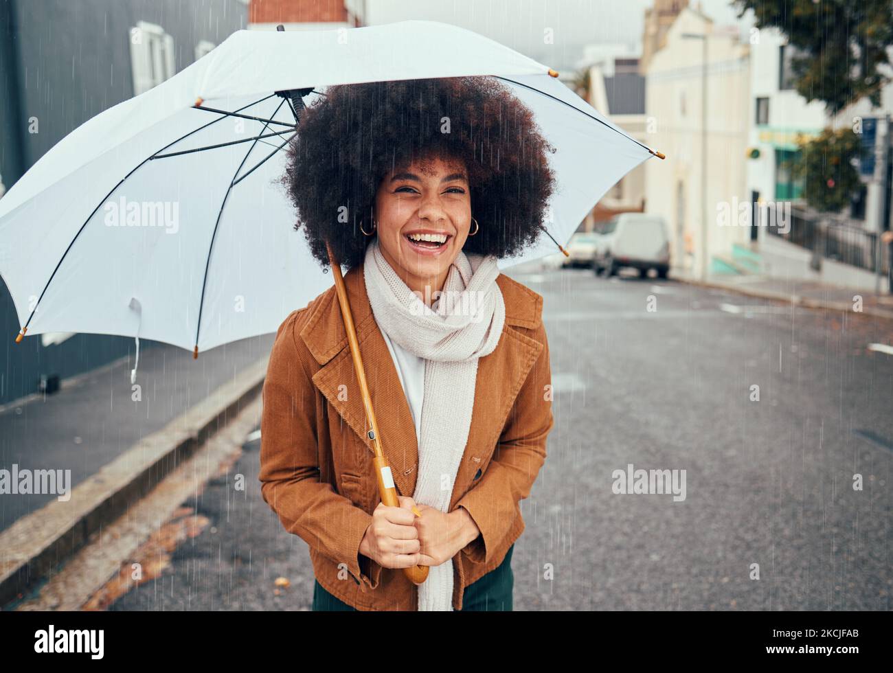 Regen, Regenschirm und Stadt mit einer schwarzen Wanderfrau an einem kalten oder nassen Wintertag auf der Straße. Wasser, Versicherung und Deckung mit einem jungen Afro-Weibchen Stockfoto