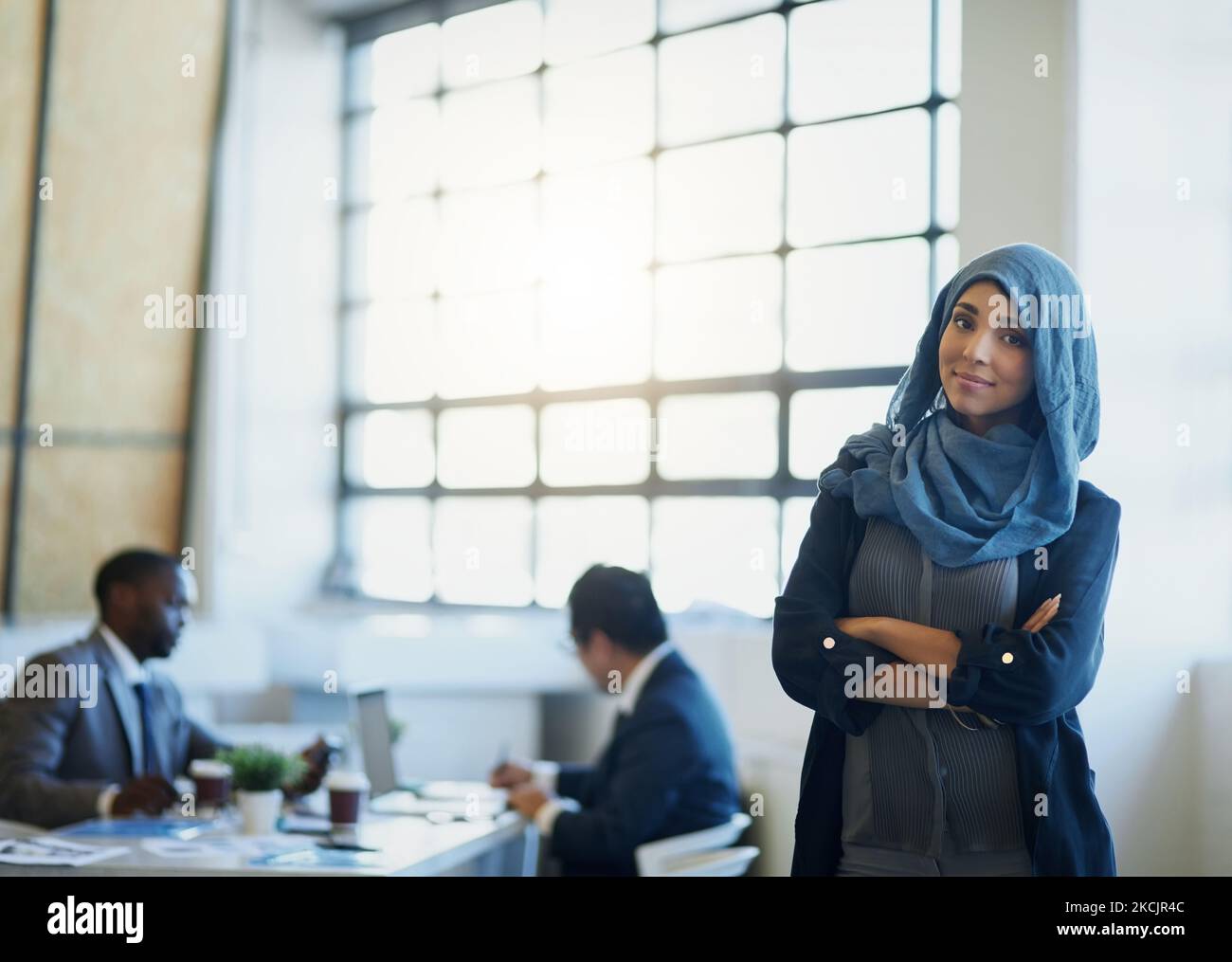 Auf harte Arbeit folgen große Verdienste. Porträt einer muslimischen Geschäftsfrau, die in einem Büro mit ihren Kollegen im Hintergrund steht. Stockfoto Auf harte Arbeit folgen große Verdienste. Porträt einer muslimischen Geschäftsfrau, die in einem Büro mit ihren Kollegen im Hintergrund steht. Stockfoto