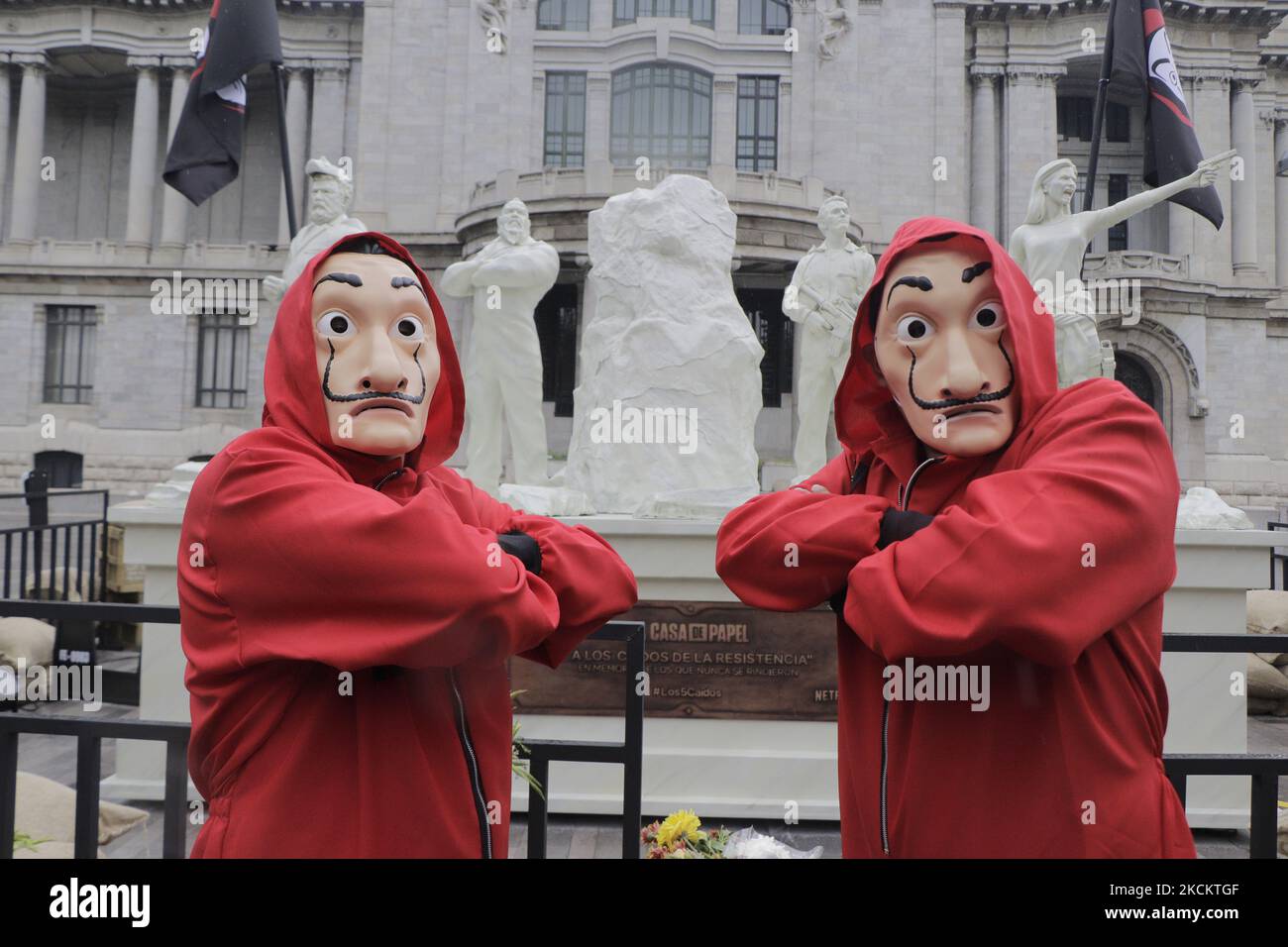 Zwei junge Männer in roten Overalls und eine Salvador Dalí Maske bewachen das Denkmal, das die 5 Gefallenen genannt wird, auf der Esplanade des Palastes der Schönen Künste in Mexiko-Stadt, vor der Premiere der fünften Staffel der Serie The House of Paper installiert. (Foto von Gerardo Vieyra/NurPhoto) Stockfoto