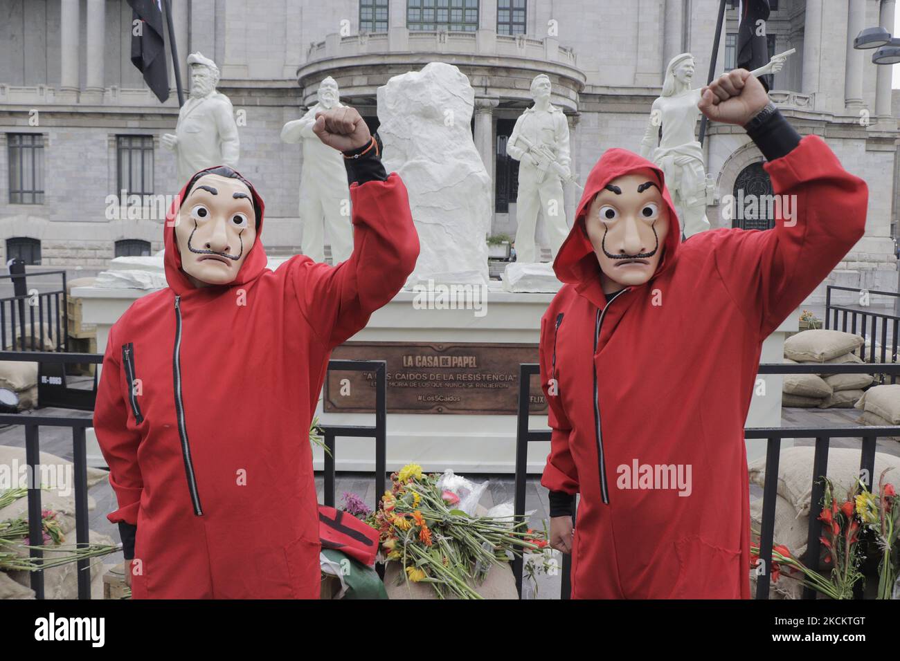 Zwei junge Männer in roten Overalls und eine Salvador Dalí Maske bewachen das Denkmal, das die 5 Gefallenen genannt wird, auf der Esplanade des Palastes der Schönen Künste in Mexiko-Stadt, vor der Premiere der fünften Staffel der Serie The House of Paper installiert. (Foto von Gerardo Vieyra/NurPhoto) Stockfoto