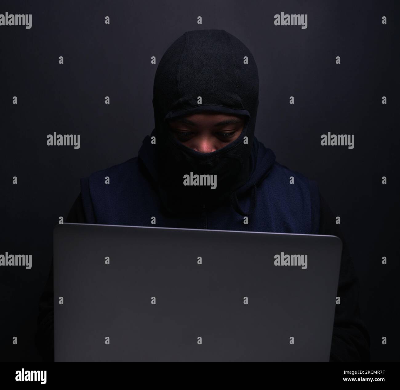 Ein Hacker, der einen Laptop vor dunklem Hintergrund benutzt. Stockfoto