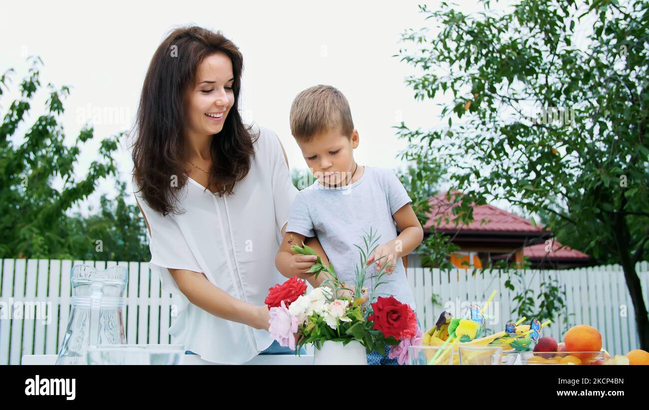 Sommer, im Garten. Mama und ein vierjähriger Sohn machen einen Blumenstrauß. Der Junge mag es sehr, er ist glücklich, hat Spaß, die Familie verbringt ihre Freizeit zusammen. Hochwertige Fotos Stockfoto