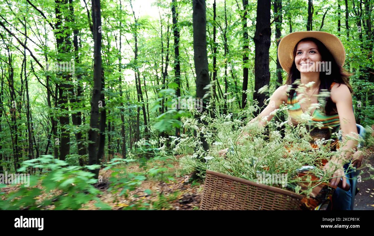 Eine Frau in einem Hut und Kleid, mit einem Korb mit Blumen, zusammen mit einem kleinen Kind, Fahrrad fahren, im Wald, im Sommer. Das Kind sitzt in einem speziellen Stuhl. Hochwertige Fotos Stockfoto