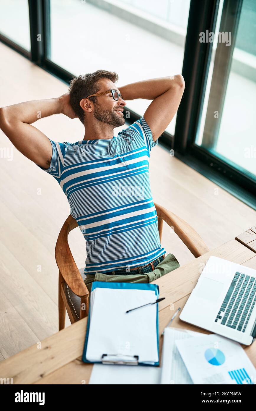 Keine Sorge in der Welt. High-Angle-Aufnahme eines hübschen jungen Unternehmers, der mit den Händen hinter dem Kopf sitzt, während er von zu Hause aus arbeitet Stockfoto