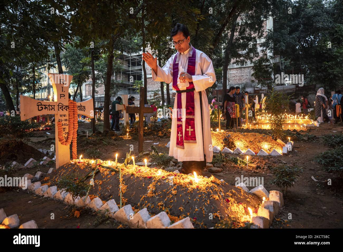 Ein Priester, der als Familie Gebete rezitiert, betet für seinen verstorbenen Verwandten, um den All Souls Day am 2. November 2021 auf einem Friedhof in Dhaka zu feiern. (Foto von Ahmed Salahuddin/NurPhoto) Stockfoto