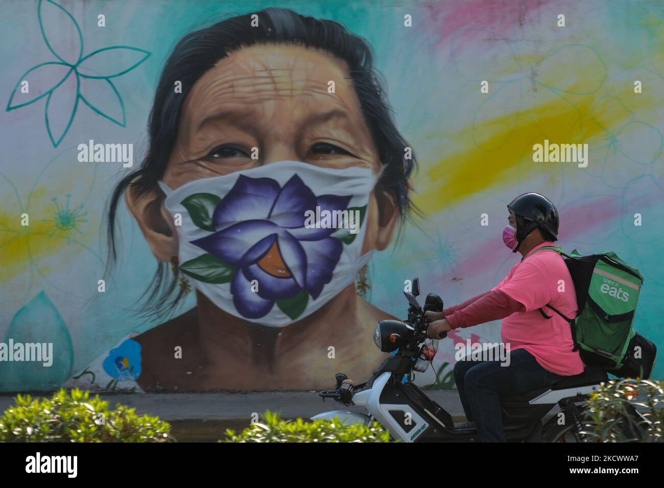 Uber Eats Courier fährt an einem Wandbild vorbei, auf dem eine Maya-Frau mit Gesichtsmaske dargestellt ist, das der mexikanische Künstler Arnold Cruz, besser bekannt als 'Datoer', im Zentrum von Merida gemalt hat. Das Kunstwerk steht in Zusammenhang mit den Pandemien von Covid-19 und soll diesen „Helden“, die ihr Leben riskieren, um das Virus zu bekämpfen, Anerkennung und Wertschätzung verleihen. Am Sonntag, 28. November 2021, in Merida, Yucatan, Mexiko. (Foto von Artur Widak/NurPhoto) Stockfoto