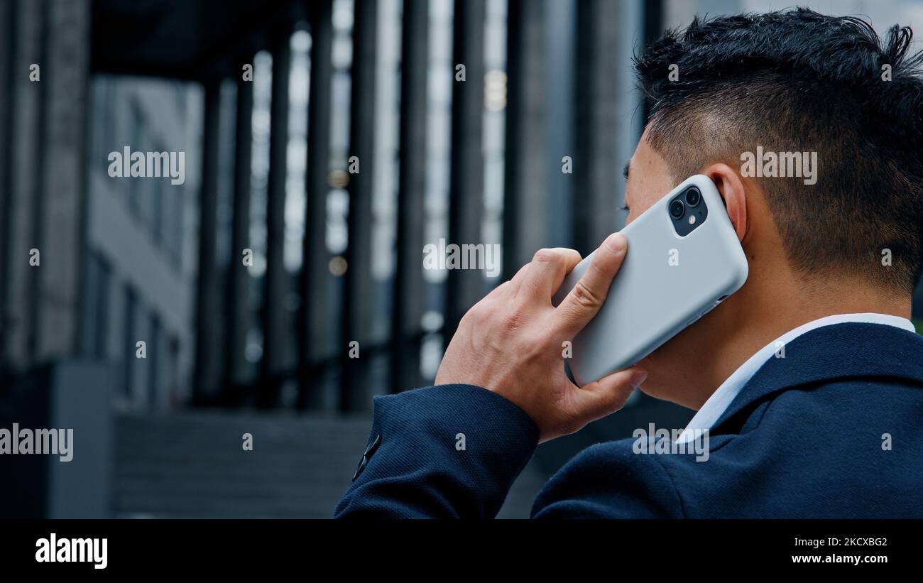 Rückansicht von hinten nicht erkennbarer asiatischer Mann in formellem Anzug, der in der Stadt steht und mit dem Smartphone telefoniert und den Chef anruft Stockfoto