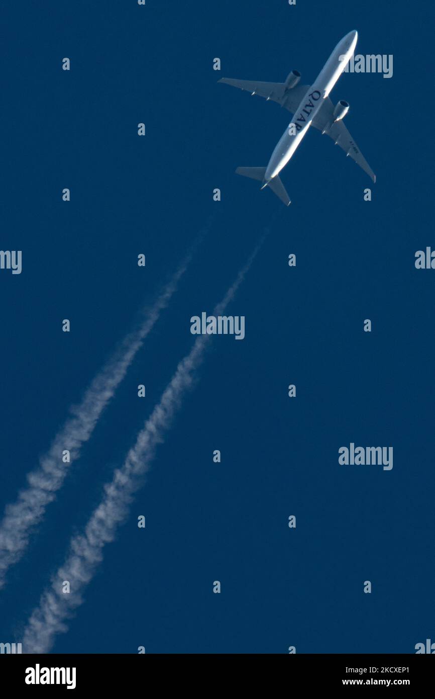 Qatar Airways Boeing 777-300ER fliegt an einem sonnigen Tag über Europa 30,000 Meter über dem blauen Himmel und fliegt von der Hauptstadt des Flughafens Doha nach London Heathrow LHR in Großbritannien. Das dreifache Sieben-B777-Überflug-Großkörper-Düsenflugzeug hat den Aufdruck MIT dem QATAR-Logo auf der Bottim des Rumpfes und hinterlässt Kondensstreifen, eine weiße Dampflinie. Das Flugzeug hat die Registrierung A7-BEK und wird von 2x GE-Motoren angetrieben. QR ist die staatliche Flaggengesellschaft von Katar, Mitglied der oneworld Airline Alliance Gruppe. Die Luftfahrtindustrie und der Personenverkehr sind p Stockfoto