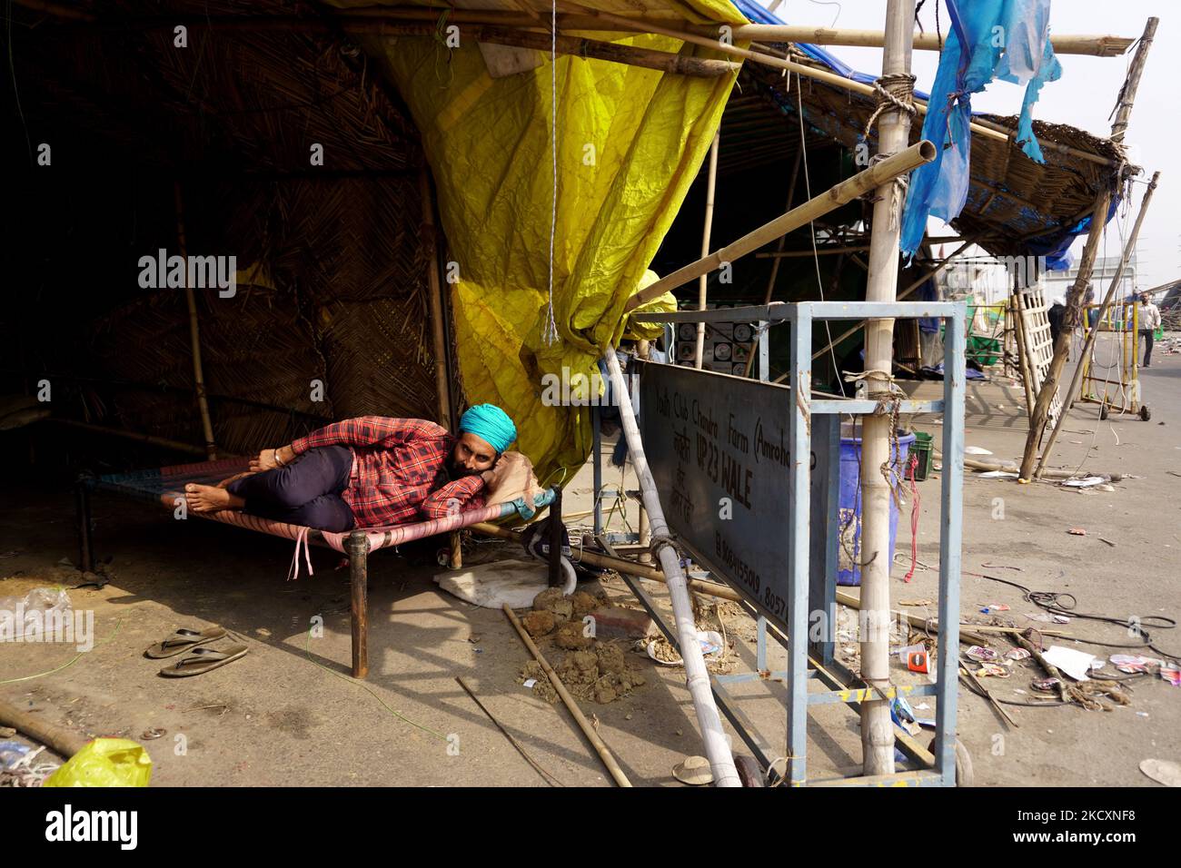 Ein Landwirt ruht sich aus, während andere temporäre Strukturen demontieren und dabei ein Protestgelände räumen, nachdem die Regierung am 12. Dezember 2021 in Ghazipur, am Stadtrand von Neu-Delhi, Indien, zugestimmt hatte, eine Reihe von Fragen zu akzeptieren, darunter die Versicherung eines Mindeststützungspreises (MSP). (Foto von Mayank Makhija/NurPhoto) Stockfoto