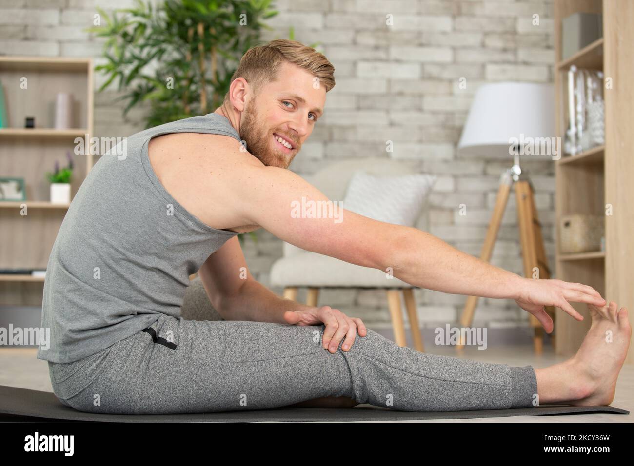 Hübscher junger Mann, der zu Hause eine Oberschenkelmuskulatur ausdehnt Stockfoto