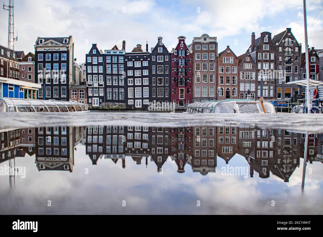 Spiegelung der liegenden Häuser. Die leeren Kanäle von Amsterdam mit den Touristenbooten dockten an. Ruhige, fast menschenleere Straßen von Amsterdam während der Sperre in der niederländischen Hauptstadt mit Geschäften und Geschäften, die mit geschlossenen Rollläden aus Metall erscheinen, Cafés, Bars und Restaurants, die auch mit geschlossenen Tischen und Stühlen der Terrassen geschlossen sind. Die Niederlande waren die erste europäische Nation, die die vollständige Sperre erklärte, um gegen die neue Omicron-Variante zu kämpfen, die aufkommt. Nach einem plötzlichen Regierungsbefehl vor Weihnachten schloss das Land all die Unessenten Stockfoto