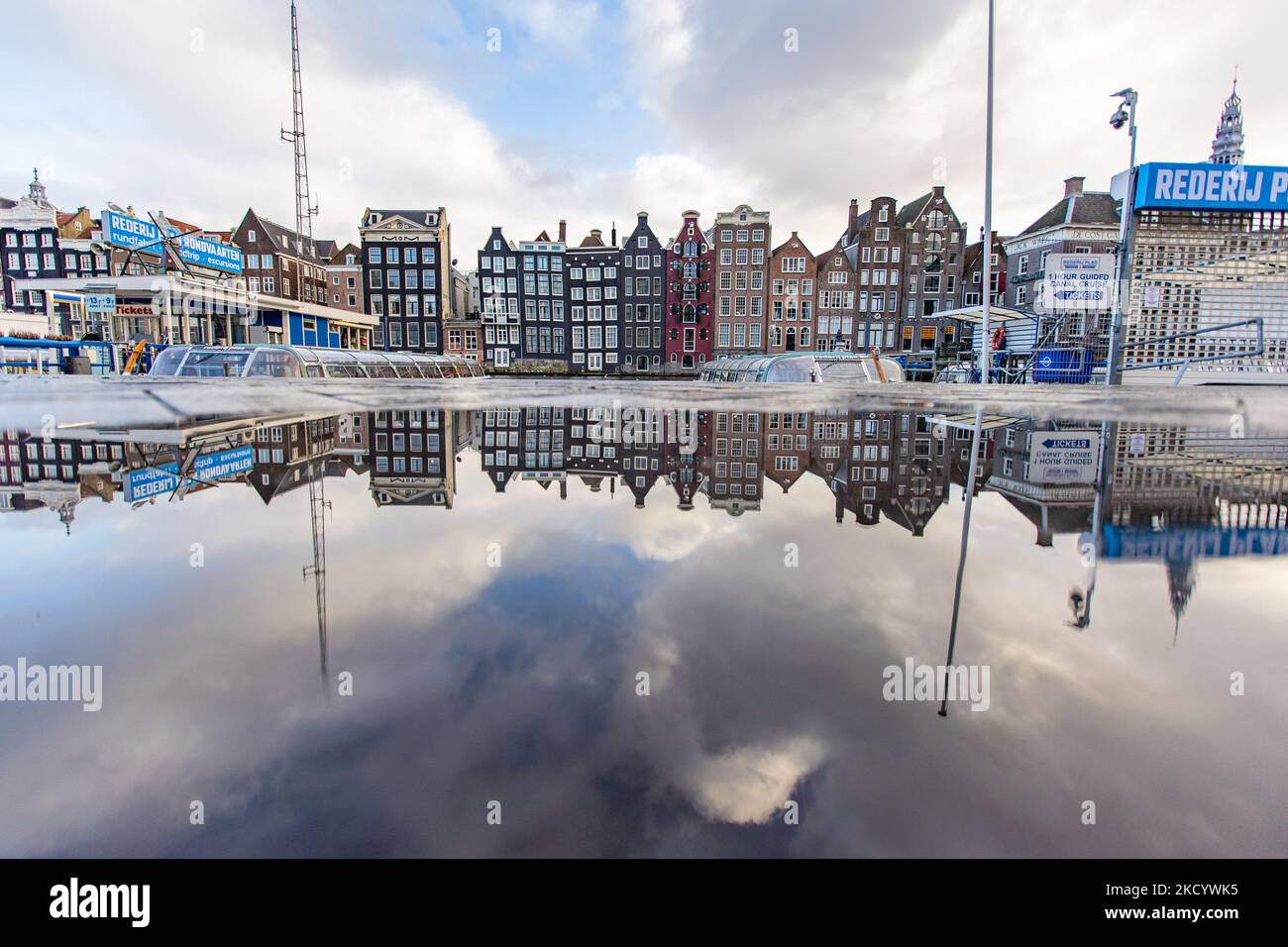 Spiegelung der liegenden Häuser. Die leeren Kanäle von Amsterdam mit den Touristenbooten dockten an. Ruhige, fast menschenleere Straßen von Amsterdam während der Sperre in der niederländischen Hauptstadt mit Geschäften und Geschäften, die mit geschlossenen Rollläden aus Metall erscheinen, Cafés, Bars und Restaurants, die auch mit geschlossenen Tischen und Stühlen der Terrassen geschlossen sind. Die Niederlande waren die erste europäische Nation, die die vollständige Sperre erklärte, um gegen die neue Omicron-Variante zu kämpfen, die aufkommt. Nach einem plötzlichen Regierungsbefehl vor Weihnachten schloss das Land all die Unessenten Stockfoto