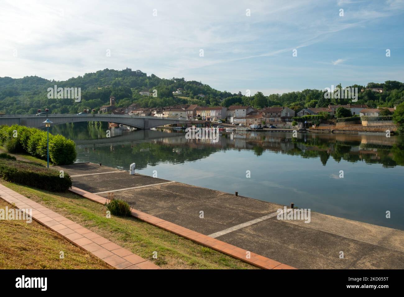 Blick über den ruhigen Fluss Lot in Richtung St-Sylvestre-sur-Lot Stadt und historischen Hügel Penne d'Agenais, Lot-et-Garonne, Frankreich vom Flussufer in Port de Penne (Penne d'Agenaise) bei Sommersonne. Stockfoto