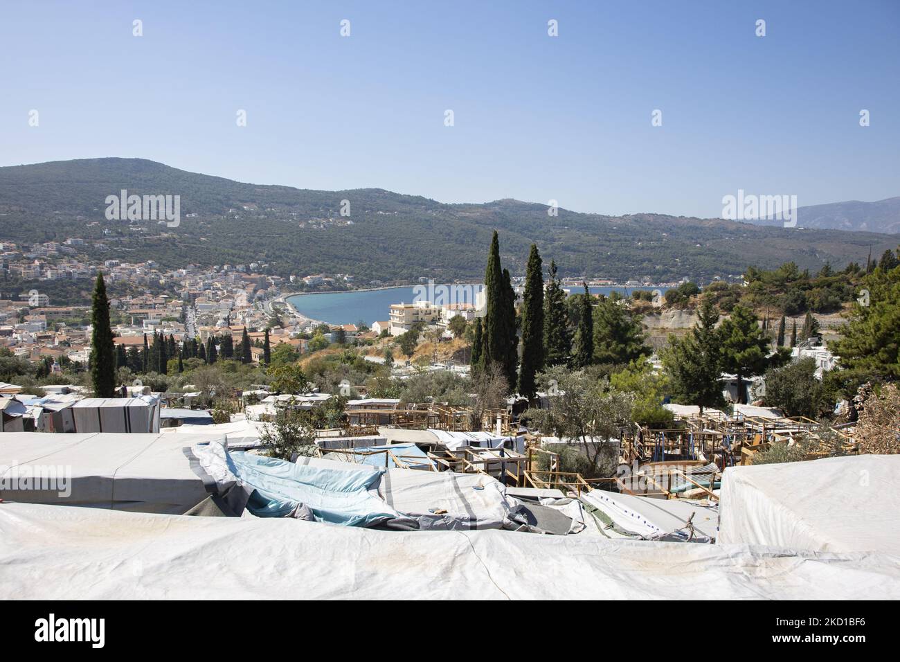 Panoramablick auf das provisorische Camp auf der Faultiere mit der Stadt und dem Hafen von Vathy sichtbar. Das ehemalige offizielle Flüchtlingslager, das von Stacheldrahtzaun auf der Insel Vathy auf Samos umgeben ist, und das benachbarte provisorische Lager mit handgefertigten Zelten und einigen von UNHCR, das sich direkt neben den Häusern der Stadt Vathi befindet, wie es als verlassen gilt. Das Lager wurde geleert und die Leute wurden umgesiedelt oder mit der Polizeieskorte in das neue Lager und einige wenige Häuser verlegt. Einmal beherbergte diese Einrichtung zu ihrer Spitze 7500 Asylbewerber in den offiziellen Einrichtungen, aber auch das provisorische Lager im Wald, das angeeknitzt war Stockfoto