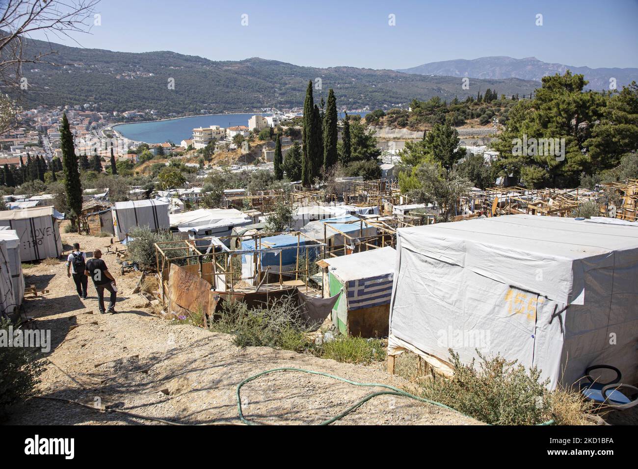 Panoramablick auf das provisorische Camp auf der Faultiere mit der Stadt und dem Hafen von Vathy sichtbar. Das ehemalige offizielle Flüchtlingslager, das von Stacheldrahtzaun auf der Insel Vathy auf Samos umgeben ist, und das benachbarte provisorische Lager mit handgefertigten Zelten und einigen von UNHCR, das sich direkt neben den Häusern der Stadt Vathi befindet, wie es als verlassen gilt. Das Lager wurde geleert und die Leute wurden umgesiedelt oder mit der Polizeieskorte in das neue Lager und einige wenige Häuser verlegt. Einmal beherbergte diese Einrichtung zu ihrer Spitze 7500 Asylbewerber in den offiziellen Einrichtungen, aber auch das provisorische Lager im Wald, das angeeknitzt war Stockfoto