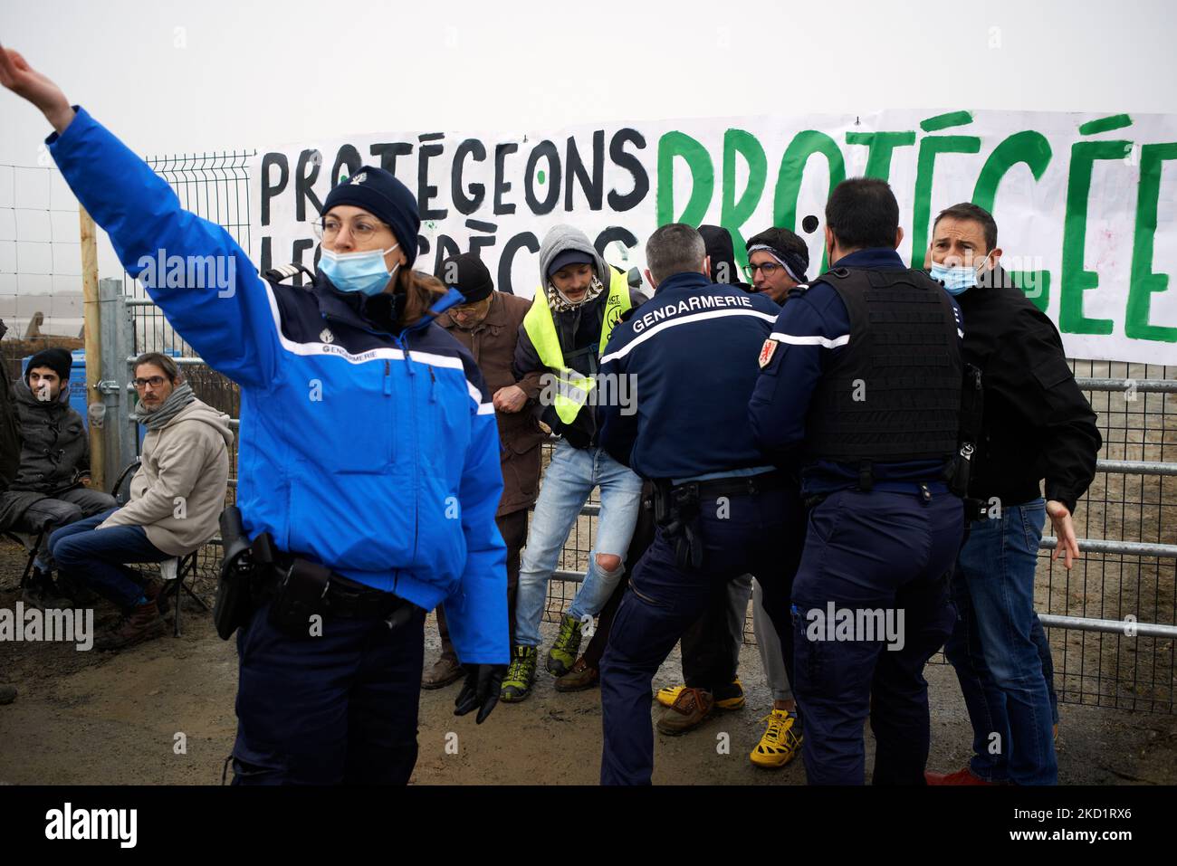 Eine Polizistin stInnen stert, als Polizisten beginnen, Aktivisten aus den Toren der Baustelle zu entfernen. Mehrere Dutzend Aktivisten von XR, ANV-COP21, ATTAC, Youth for Climate versammelten sich in Saint Sulpice La Pointe, um die Baustelle des riesigen Lagerhauses von Terra2 zu blockieren. Sie lehnen ein riesiges Lager ab, das für Amazon oder Alibaba geplant ist und mehrere landwirtschaftliche Felder abdeckt. Die Haupthalle sollte 533 m lang, 125m breit und 17m hoch sein und würde in den Top 10 der größten Lagerhäuser in Frankreich sein. Die Bauarbeiten hätten diesen Winter nicht beginnen sollen, wie Stopp Terra2 gefordert hat Stockfoto