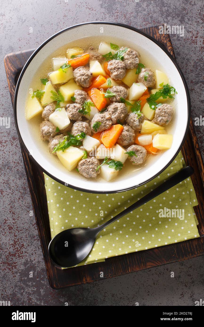 Traditionelle norwegische Suppe Sodd mit Wurzelgemüse und Fleischbällchen aus der Nähe auf einem Teller auf dem Tisch. Vertikale Draufsicht von oben Stockfoto