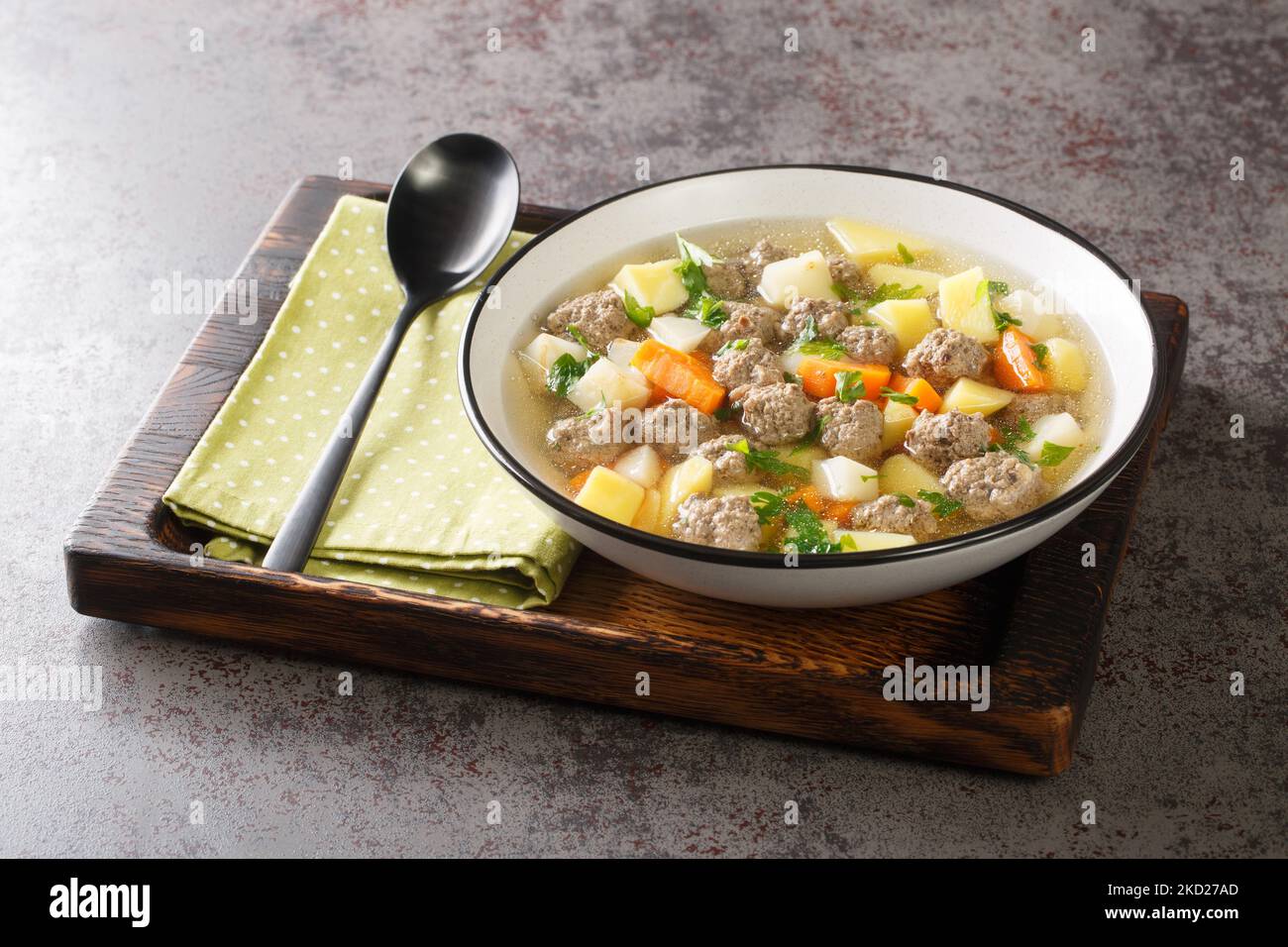 Köstliche Suppe mit Wurzelgemüse und Fleischbällchen in einer klaren Brühe in Nahaufnahme auf einem Teller auf dem Tisch. Horizontal Stockfoto