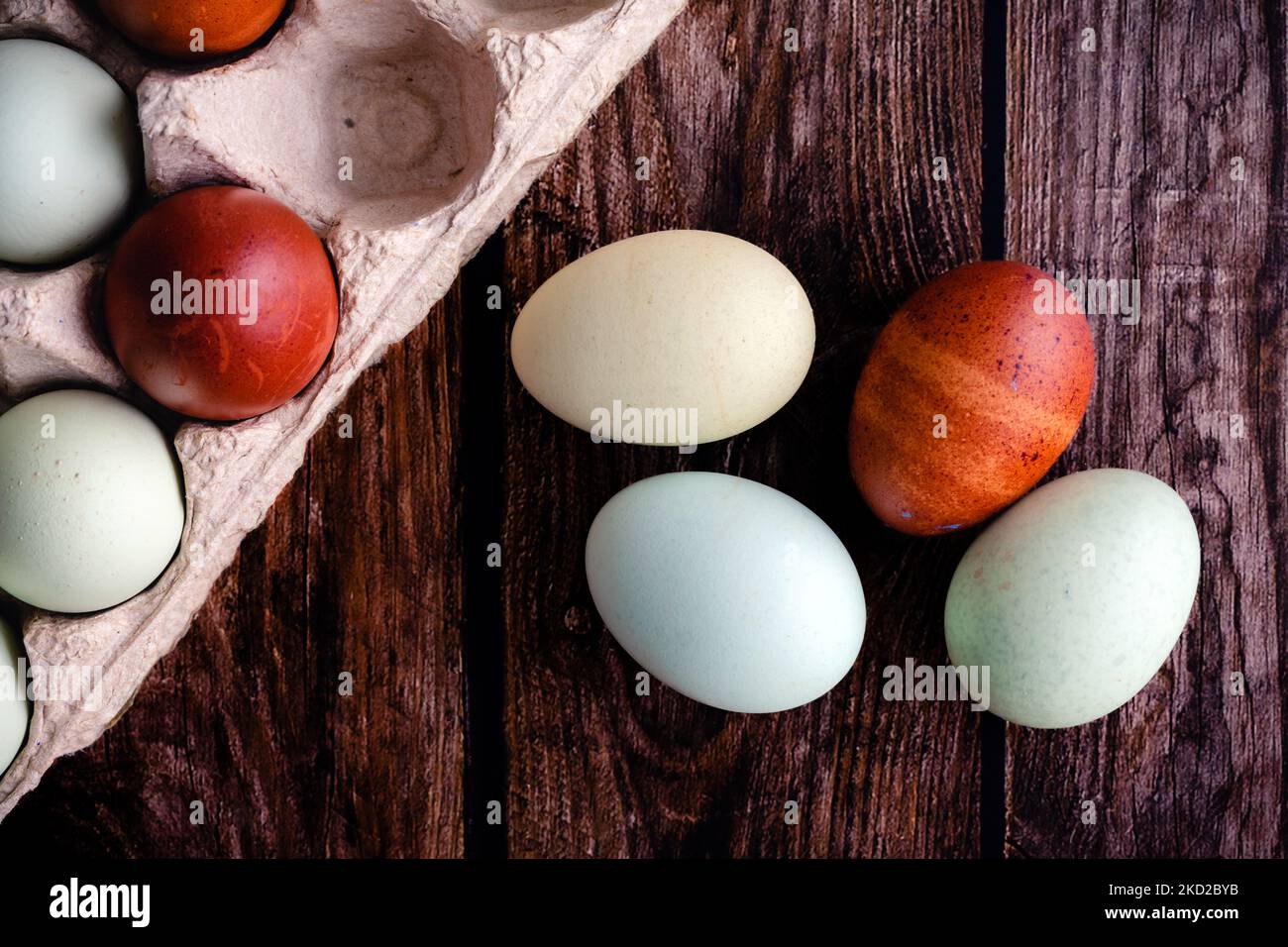 Blue, Green, and Brown Heritage Eggs with an Egg Carton on on on a Rustic Wood Background: Overhead-Ansicht einer Gruppe von bunten Eiern auf einem Holztisch Stockfoto