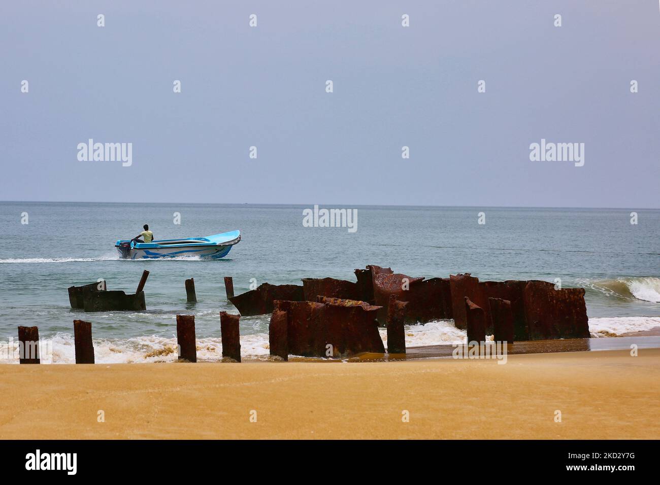 Tamilischer Mann fährt am Strand in Mullaitivu, Sri Lanka, mit einem Boot an den verrosteten Metallresten des Farah 3-Schiffes vorbei. Dies ist eine der vielen Narben aus dem 26-jährigen Bürgerkrieg zwischen der srilankischen Armee und der LTTE (Liberation Tigers of Tamil Eelam). Die Farah 3 war ein jordanisches Handelsschiff. Während er sich von der indischen Küste Andhra Pradesh nach Südafrika auf dem Weg befand, kam es zu Motorenunruhe und musste vor der Küste von Mullaitivu ankern. Die LTTE Sea Tigers entführten das Schiff und nahmen seine Besatzung im Dezember 2006 gefangen und schleppten das Schiff näher an den CO heran Stockfoto