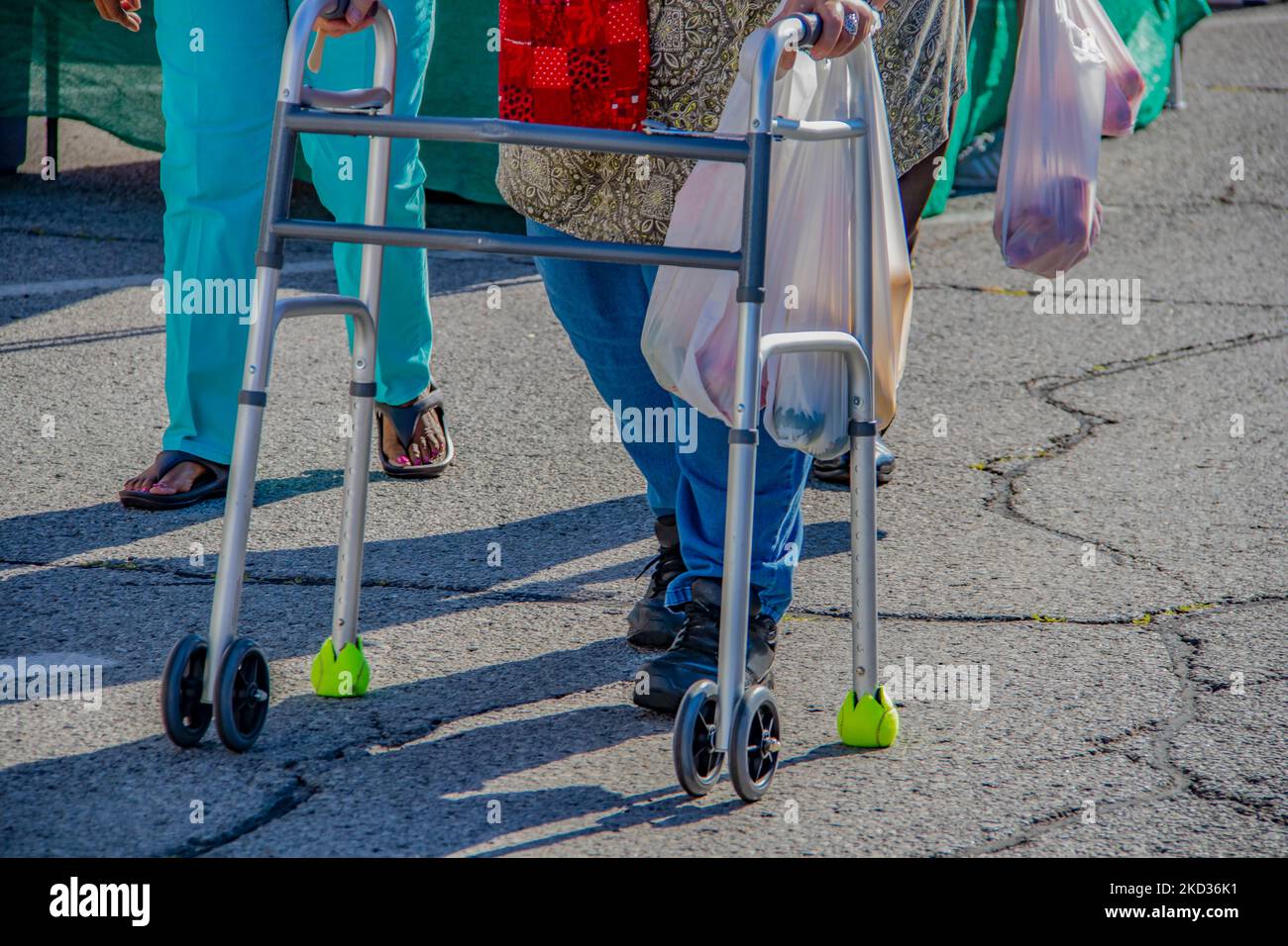 Verkürzte Beine einer Frau mit Gehhilfe auf einer asphaltierten Straße mit einem Beutel mit Produkten auf dem Bauernmarkt Stockfoto