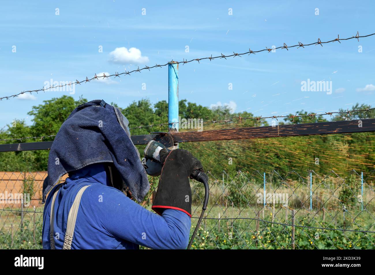 Ein Arbeiter in der Schwerindustrie schleift Schweißnähte mit einem elektrischen Winkelschleifer auf seiner Baustelle. Die Maske und die Schutzhandschuhe schützen vor Funken in den Augen und Stockfoto