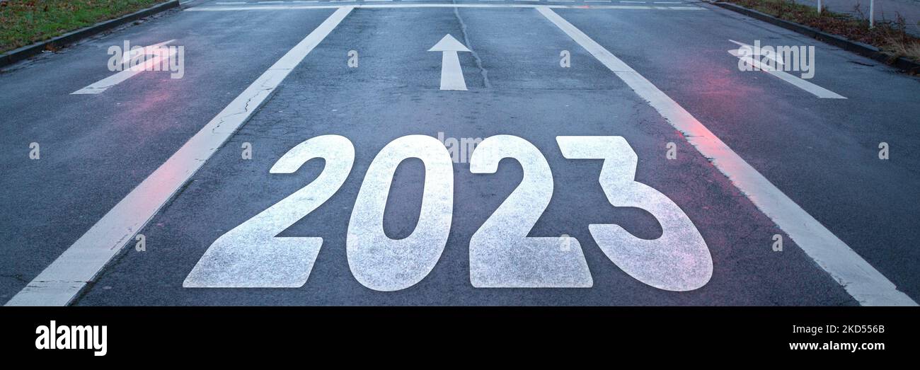 Detail einer Asphaltstraße mit Pfeilen auf der Fahrspur und der Aufschrift „2023“ auf der geraden Fahrspur als Symbol für das künftige Jahr Stockfoto